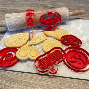 Koekjes en rode bakvormpjes met de vormen van verschillende BDSM speeltjes