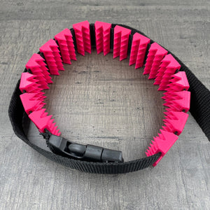 Een BDSM cilice met een zwarte band en spikes in de kleur magenta