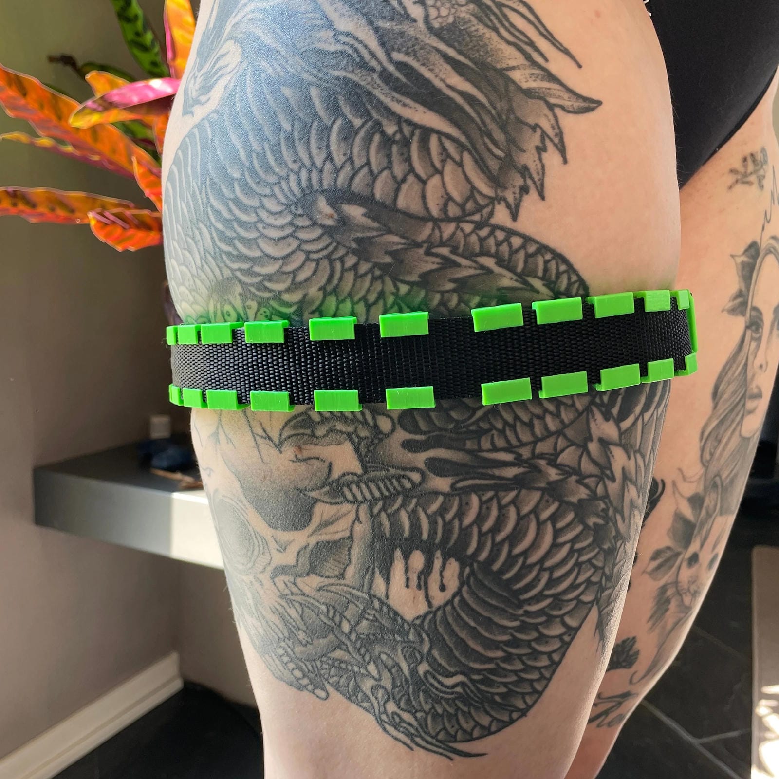 Een BDSM cilice met een zwarte band en groene spikes om de been van een persoon