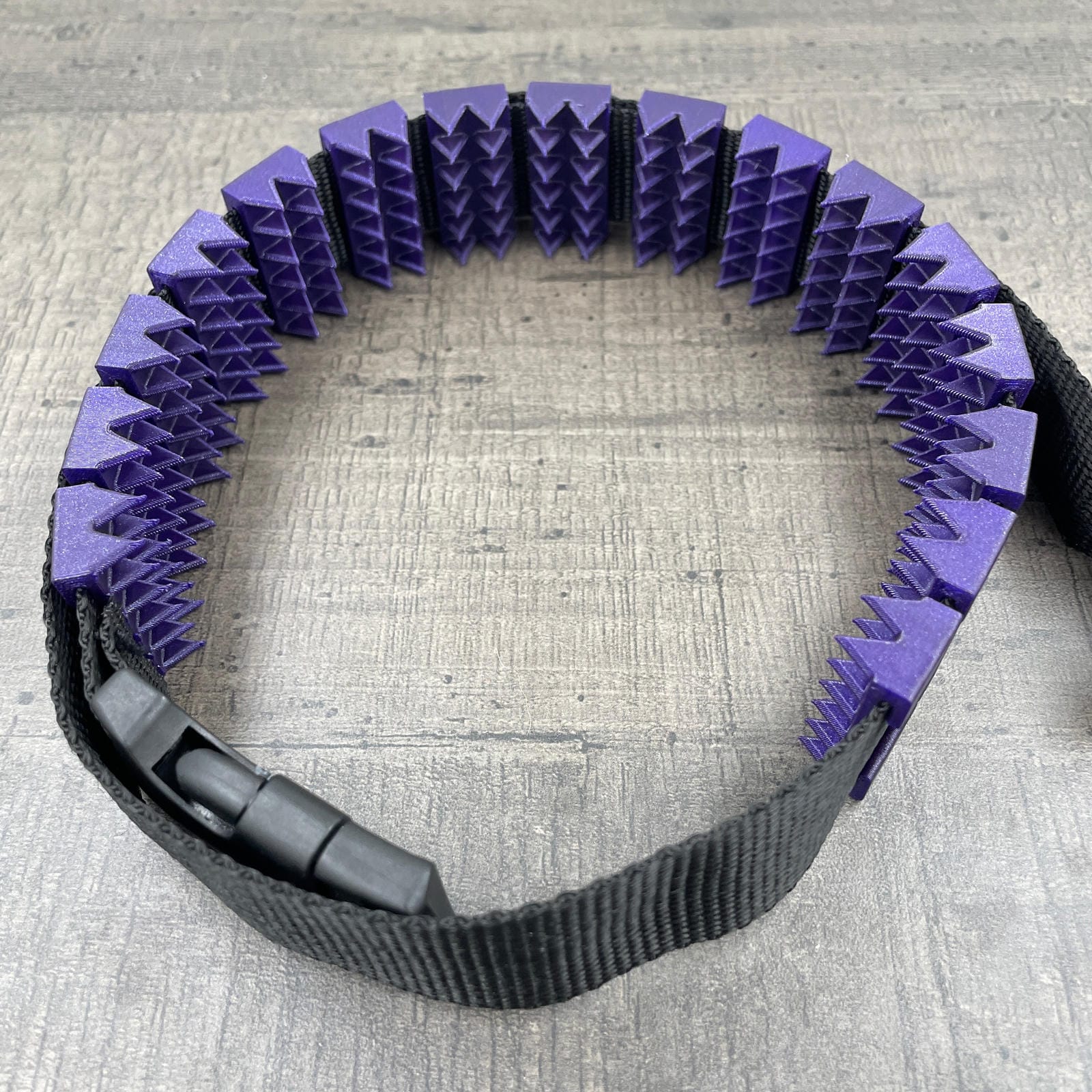 Een BDSM cilice met een zwarte band en spikes in de kleur paars met glitters