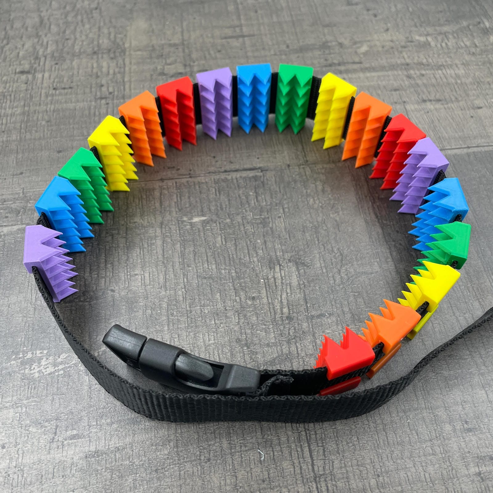 Een BDSM cilice met een zwarte band en spikes in de kleuren van de regenboog