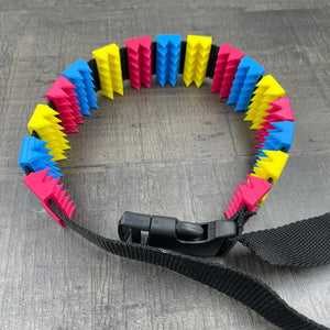 Een BDSM cilice met een zwarte band en spikes in de kleuren van de non-binaire vlag