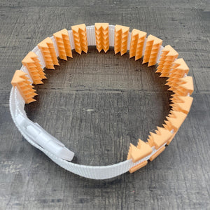 Een BDSM cilice met een witte band en oranje spikes