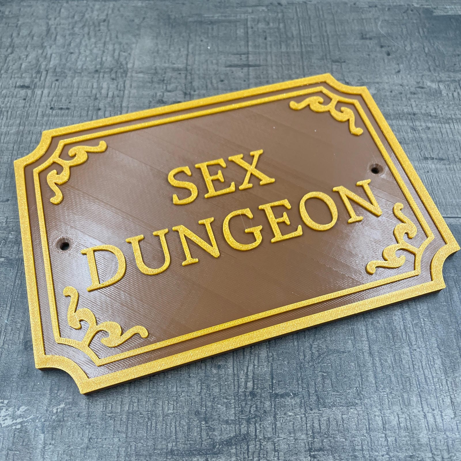 Een bruin deurbordje met de tekst "Sex Dungeon" in gouden letters.